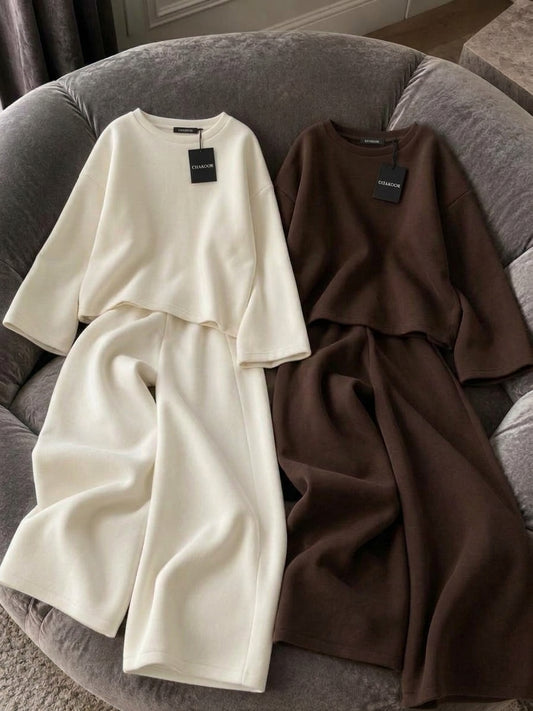 This image showcases a detailed flat lay of a minimalist 2-piece set featuring a relaxed oversized crewneck top and fluid wide-leg trousers in a rich maroon color. It is crafted from premium plain fleece fabric with a clean drape. It is presented on a plush grey velvet armchair under soft directional lighting. Perfect for modern streetwear, cafe hangouts, and airport looks. Secure this unique aesthetic with confidence from CHAKOOR, an authentic online store.BROWN WHite