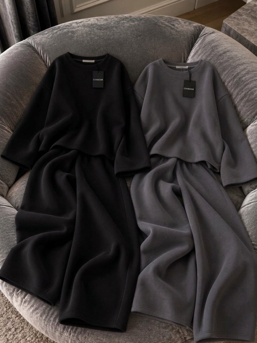 This image showcases a detailed flat lay of a minimalist 2-piece set featuring a relaxed oversized crewneck top and fluid wide-leg trousers in a rich maroon color. It is crafted from premium plain fleece fabric with a clean drape. It is presented on a plush grey velvet armchair under soft directional lighting. Perfect for modern streetwear, cafe hangouts, and airport looks. Secure this unique aesthetic with confidence from CHAKOOR, an authentic online store.