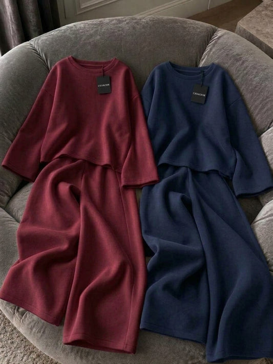 This image showcases a detailed flat lay of a minimalist 2-piece set featuring a relaxed oversized crewneck top and fluid wide-leg trousers in a rich maroon color. It is crafted from premium plain fleece fabric with a clean drape. It is presented on a plush grey velvet armchair under soft directional lighting. Perfect for modern streetwear, cafe hangouts, and airport looks. Secure this unique aesthetic with confidence from CHAKOOR, an authentic online store.